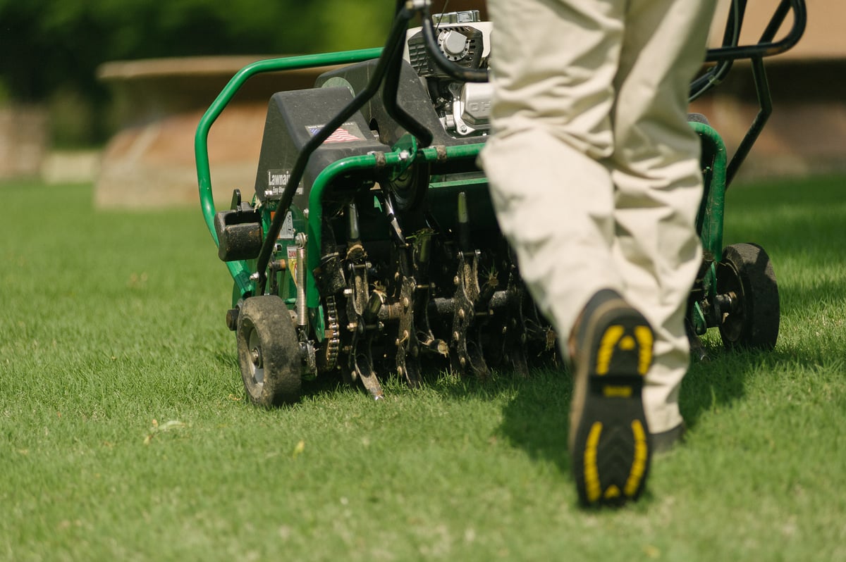 lawn care technician aerates lawn with walk behind machine