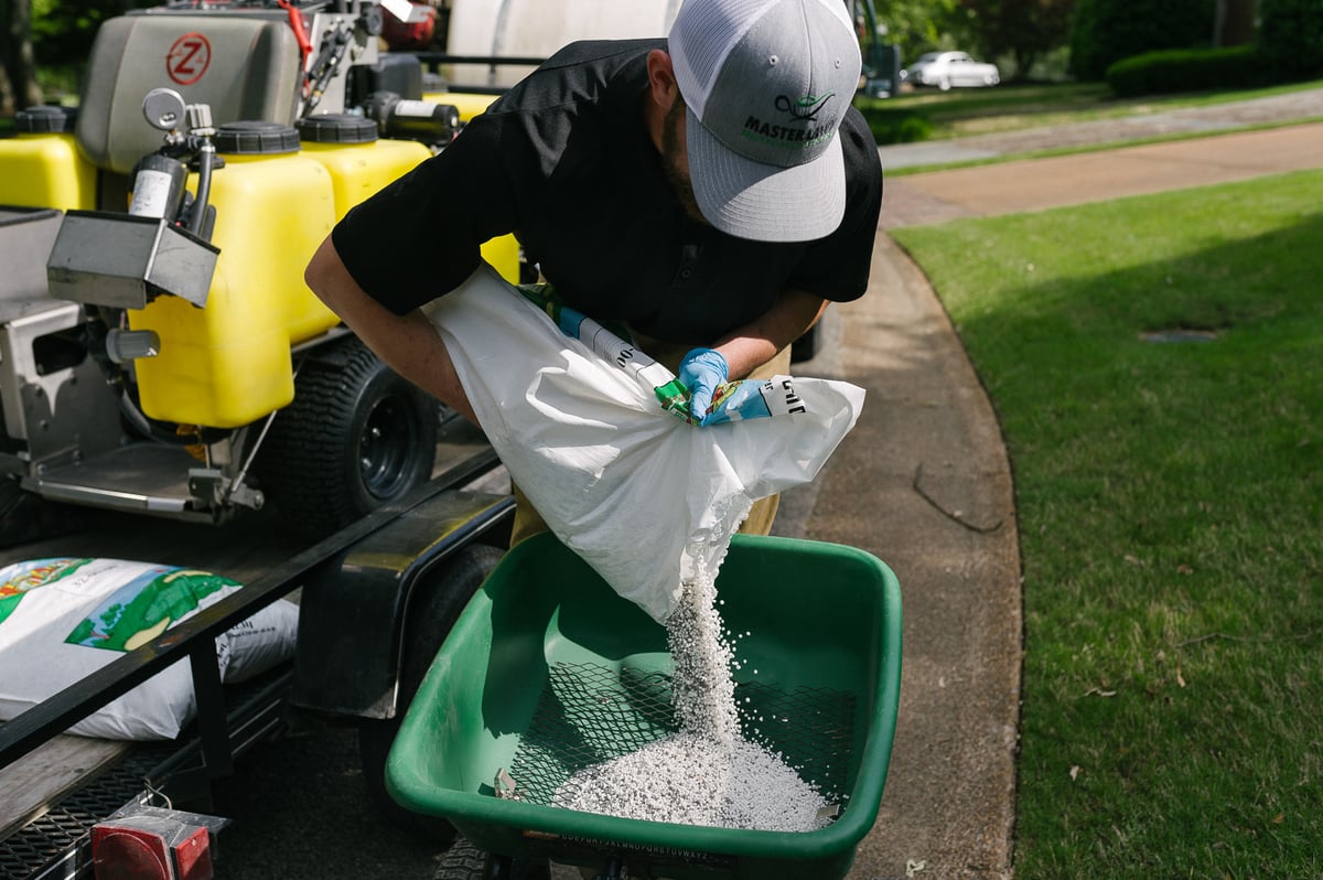 technician pours granular fertilizer into spreader