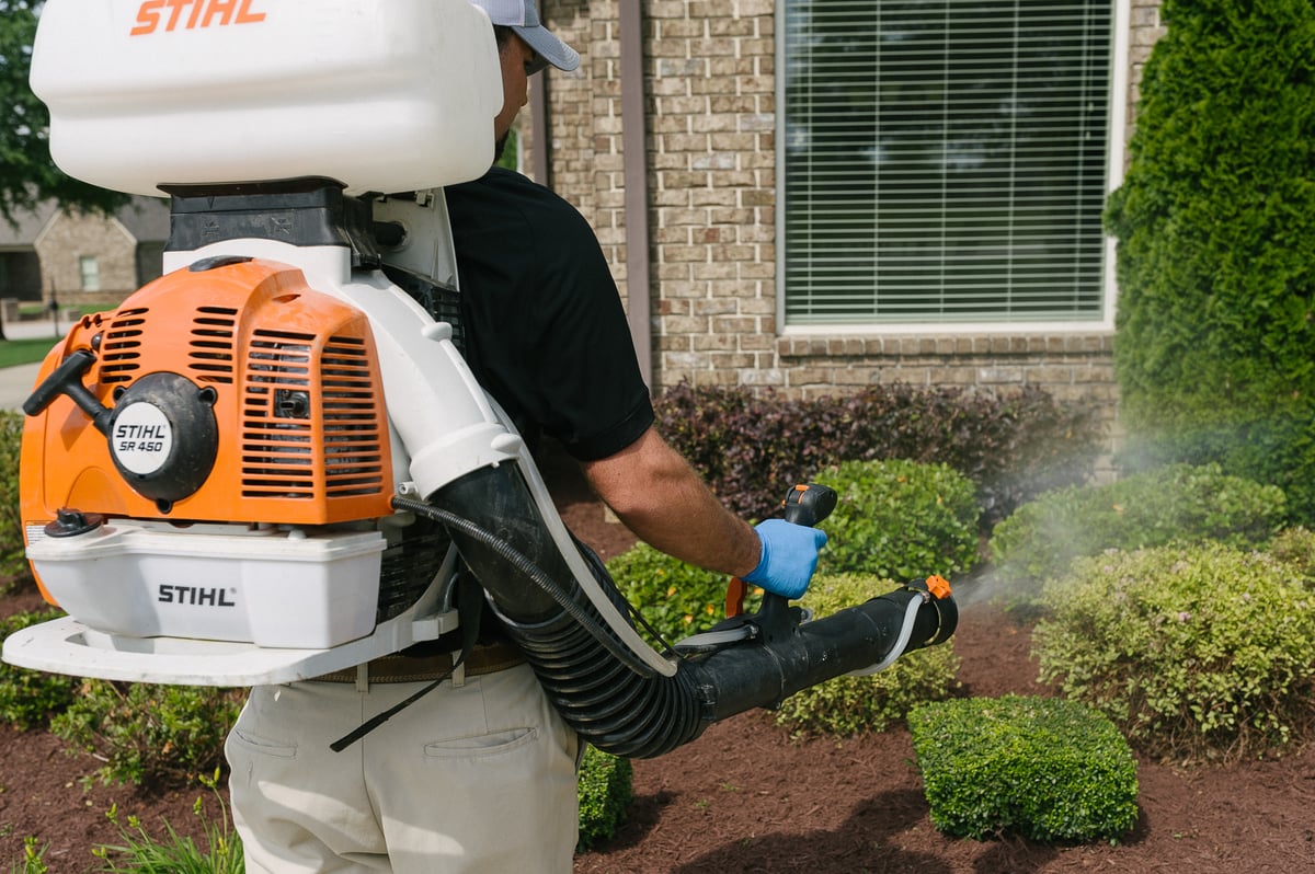 mosquito control technician spraying landscape beds at home for pests 